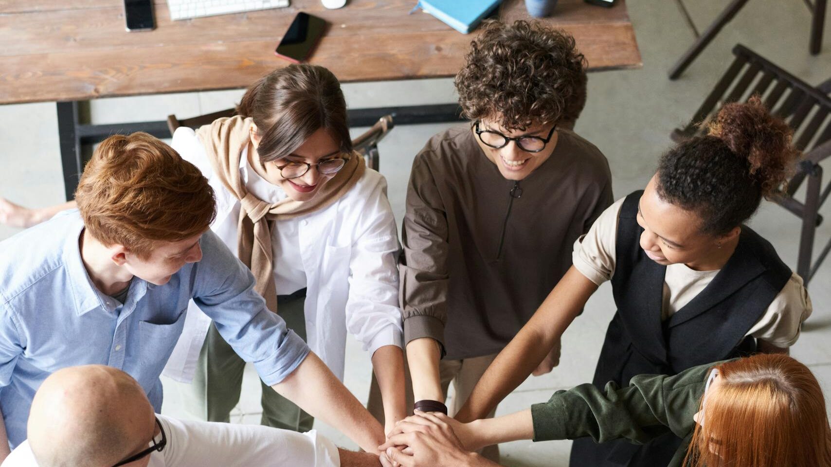 A diverse group of professionals joins hands in a team-building exercise indoors.